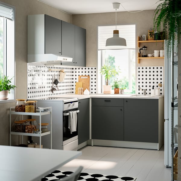 Moderne L-förmige Küche mit dunkelgrauen Schränken, schlanken Arbeitsplatten und offenen Regalen mit Topfpflanzen und Kaffeezubehör.