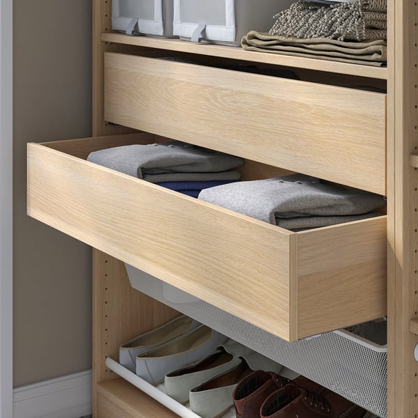 Eine offene Holzschublade aus der IKEAS KOMPLEMENT-Serie, gefüllt mit gefalteten grauen Pullovern in einem hellen Kleiderschrank.