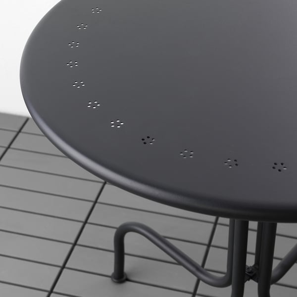 Runder schwarzer Outdoor-Tisch mit strapazierfähiger, pulverbeschichteter Stahloberfläche und robusten Metallbeinen auf Fliesenboden.