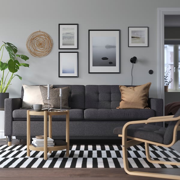 Gemütliches graues LANDSKRONA Sofa mit Holzbeinen. Es ist groß, mit Kissen und einem Couchtisch in der Nähe. Kunstwerke und eine Pflanzendekoration das moderne Wohnzimmer.
