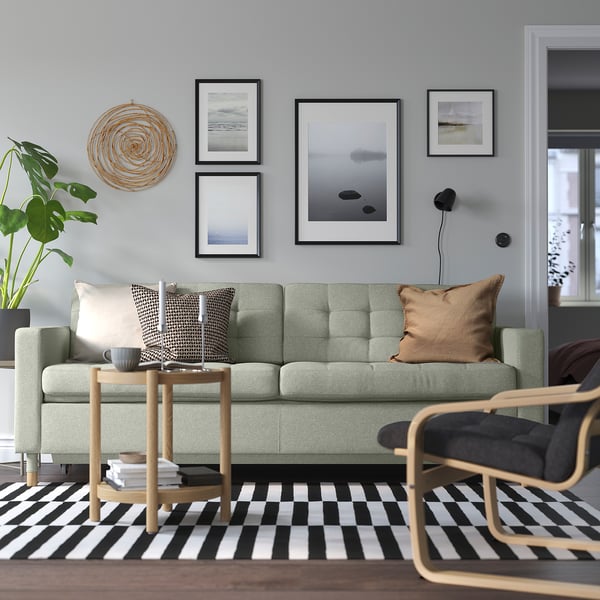 Modernes Wohnzimmer mit grünem Sofa LANDSKRONA. Couchtisch aus Eiche, gestreifter Teppich und Wandkunst. Das Sofa ist groß, mit Kissen und Kissen.