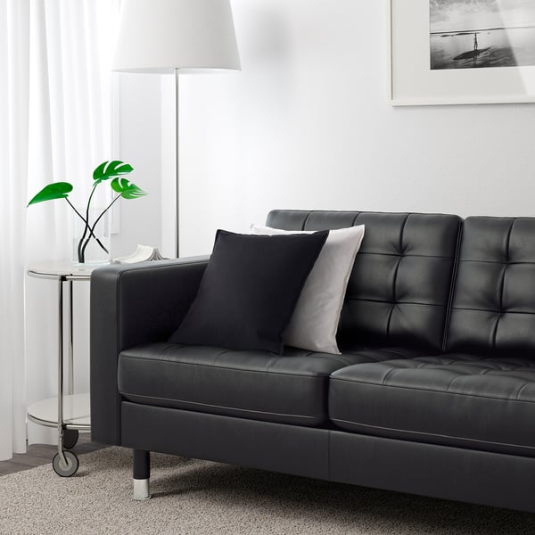 Ein modernes dunkelgraues Ecksofa mit getufteter Rückenlehne und Sitzkissen, abnehmbaren Armlehnen und einer hohen Stehlampe daneben.