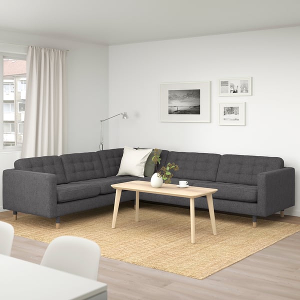 Modernes Wohnzimmer mit großem, dunkelgrauem L-förmigem Sektionssofa als Mittelstück, hellem Couchtisch aus Holz, beigem Teppich und Wandfotos.