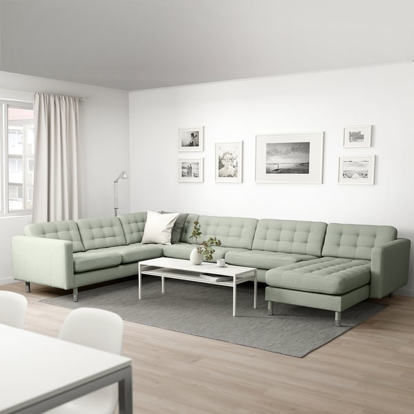 Modernes Wohnzimmer mit grüner LANDSKRONA-Sektion, weißem Couchtisch, Wandkunst, Stehlampe, warmem Teppich und Holzboden.