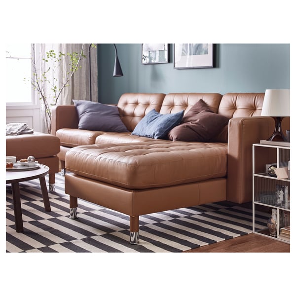 Modernes Wohnzimmer mit braunem Ledersofa, Kissen, gestreiftem Teppich, Beistelltisch, Lampe und Bücherregal.