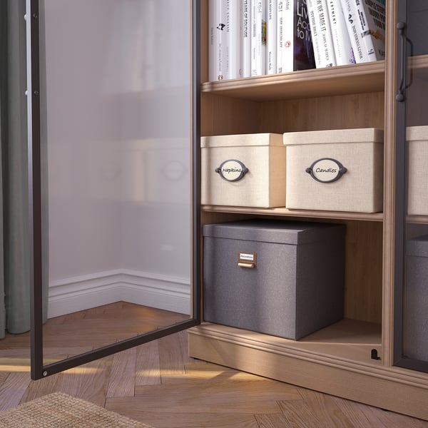 In der Vitrine mit Glastür sind Bücher und Schachteln mit Metallgriffen und Holzregalen ausgestellt, die an der Wand befestigt sind.