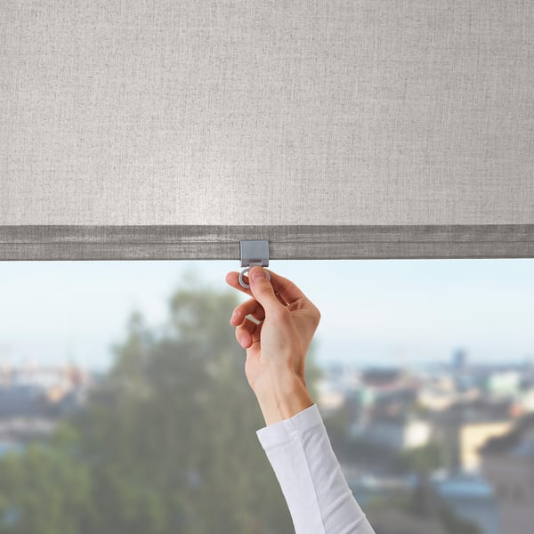 Eine Hand stellt ein Rollo ein und demonstriert damit seine kabellose Funktion. Die Jalousie filtert das Licht und sorgt so für Privatsphäre, während sie zu hohen Fenstern passt.
