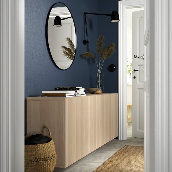 Flur mit LAPPVIKEN Eichenschrank, Spiegel, Wandlampen, Pflanzen, Büchern, Korb darunter. Blaue Wand, schlankes Design.