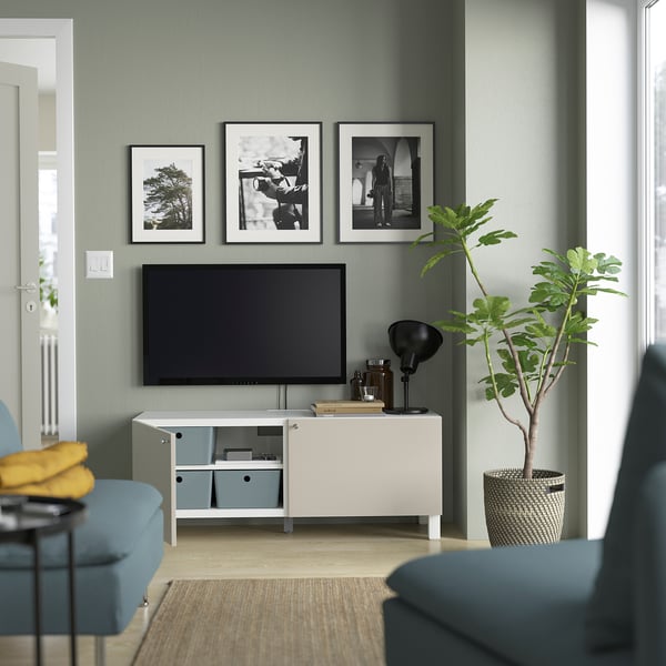 Modernes Wohnzimmer mit Flachbildfernseher auf elegantem Medienständer. Graue Wände, blaue Couch und Zimmerpflanze. Über ihm hängen drei gerahmte Schwarz-Weiß-Fotos.