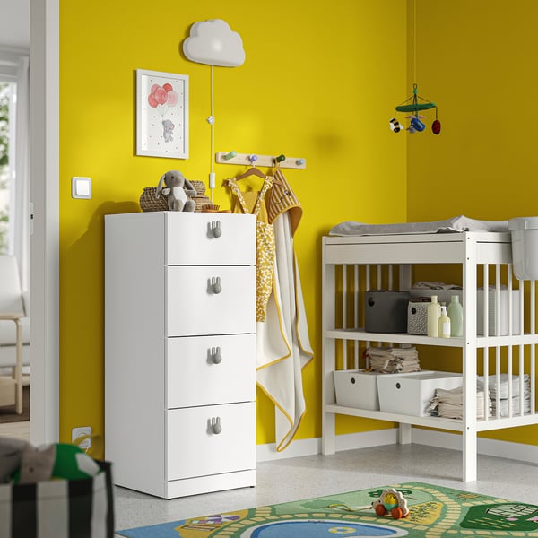 Helles Kinderzimmer mit weißer LASTARE-Brust , gelben Wänden. Truhe hoch mit vier Schubladen, grauen Griffen, in der Nähe eines weißen Wickeltisches.