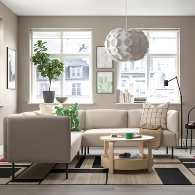 Modernes Wohnzimmer mit beigem LILLEHEM-Sofa, grünen Kissen, Couchtisch aus Holz, Teppich, Stehlampe und Topfpflanze am Fenster.