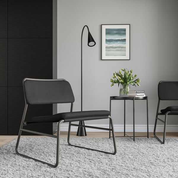 Minimalistischer Wohnraum mit schwarzen LINNEBÄCK-Stühlen, modernem Beistelltisch, eleganter Lampe und floraler Vase. Kunstwerk an der Wand. Gemütliche, moderne Einrichtung.
