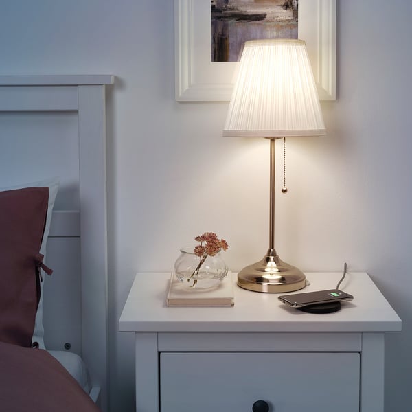 Nachttisch mit weißer Lampe, Buch, Vase und Telefon.