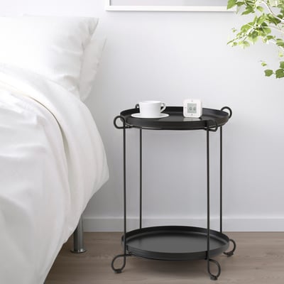 Schwarzer Beistelltisch mit Tabletts im minimalistischen Schlafzimmer, mit Tasse und Gadget.