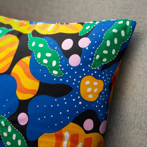 Farbenfroher, abstrakter Blumenkissenbezug mit grünen gepunkteten Blättern, genäht auf einer grauen gepolsterten Oberfläche.