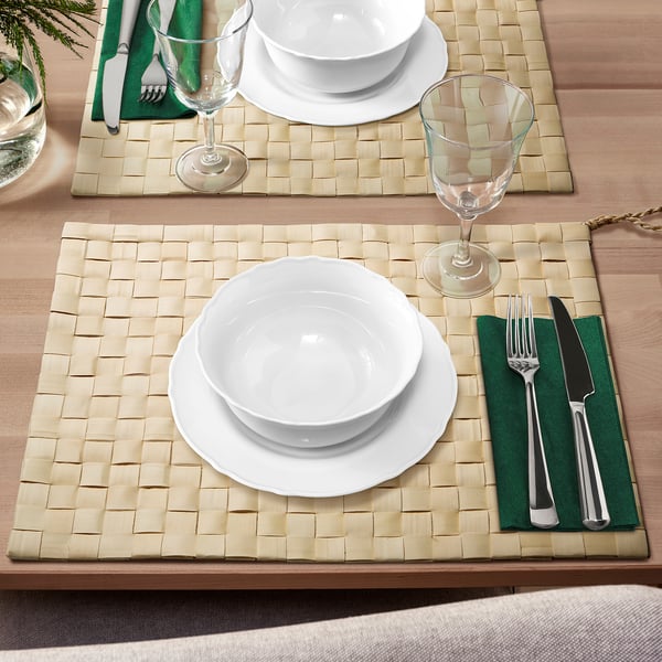 Beige MÄVINN Tischsets mit Palmblatt-Design, mit weißem Geschirr und Gläsern, grünen Servietten, warmer Tischdekoration.