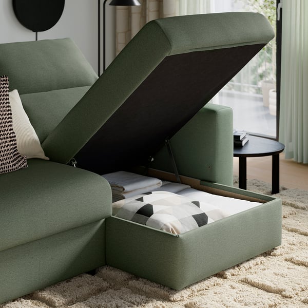 Grünes Sofa mit offenem Abstellfach, gefüllt mit Kissen und Decken.