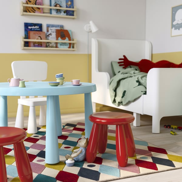 Kinderspielbereich mit blauem Tisch, roten Hockern. Heller Teppich, weißer Stuhl.