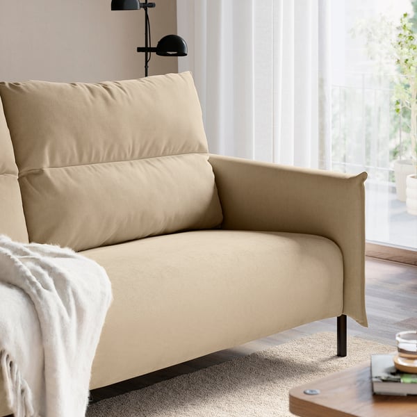 Ein beigefarbenes, hochlehniges Sofa mit gefalteten Armlehnen, Kissen und schwarzen Metallbeinen, das ein entspanntes und modernes Design bietet.