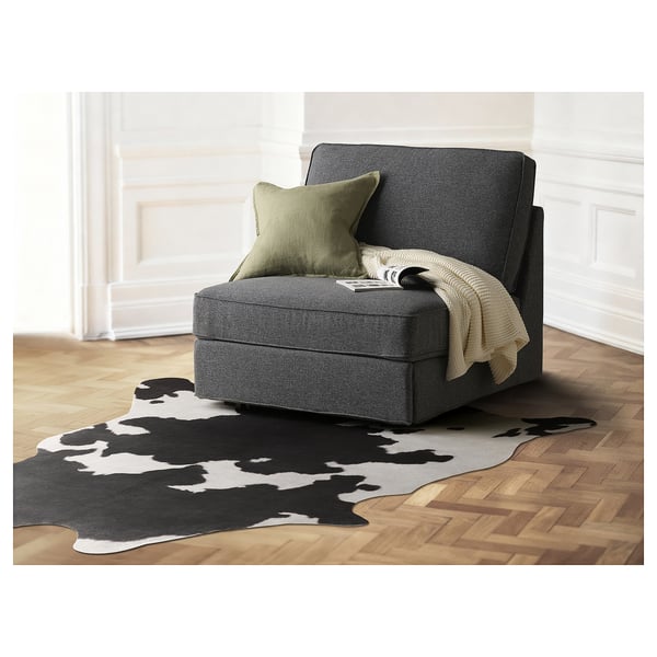 Modernes Wohnzimmer mit grauem MAXTAXA-Stuhl , olivfarbenem Kissen, Decke und Kuhlederteppich auf Holzboden.