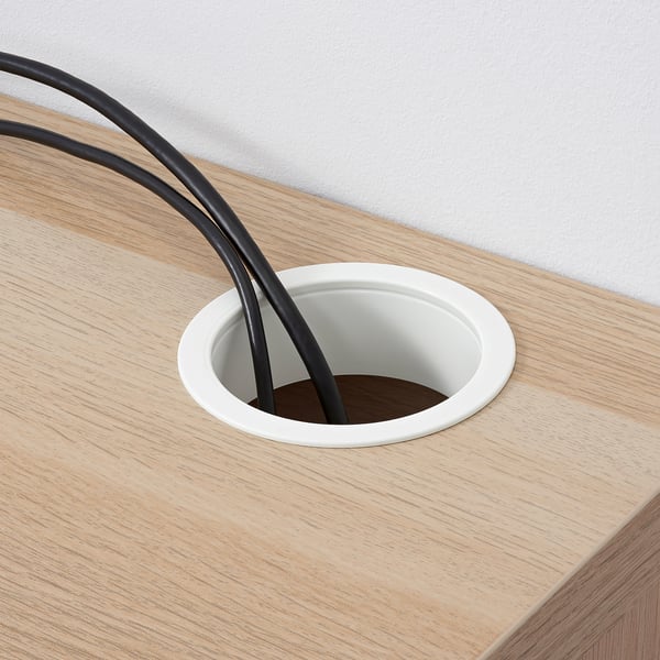 Schreibtisch aus Holz mit einem runden Kabelauslass, der zwei schwarze Kabel zeigt, die aus einer weißen Steckdose austreten und den Kabelsalat bewältigen.