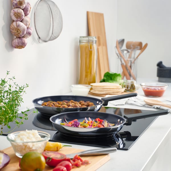MIDDAGSMAT Bratpfannen kochen auf modernen Herdplatten, umgeben von frischen Zutaten und Küchengeräten.