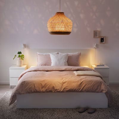 Gemütliches Schlafzimmer mit handgeflochtener Bambus-Pendelleuchte, beiger Bettwäsche und minimalistischem Dekor.