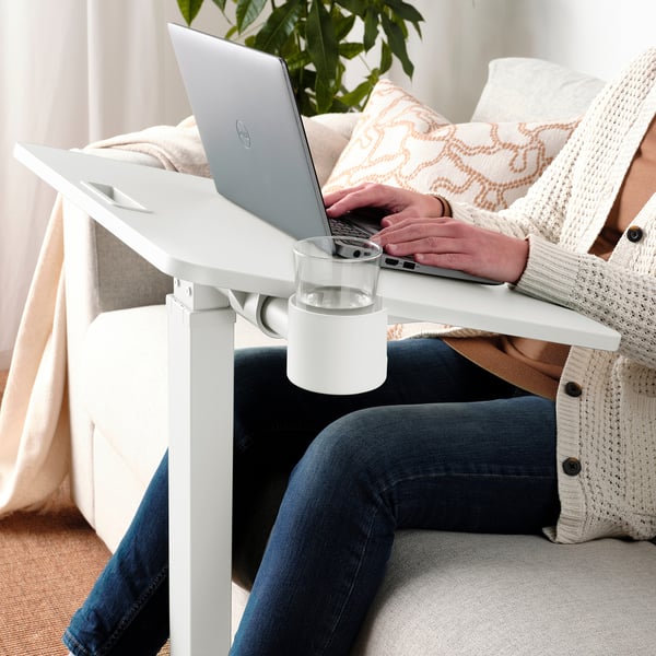 Person mit verstellbarem Laptoptisch mit Getränk, auf gemütlicher Couch.