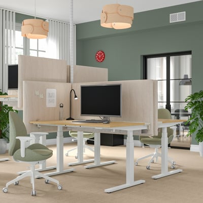 Modernes Büro mit MITTZON Sitz-Steh-Schreibtischen und grünen Stühlen. Sanftes Licht und große Fenster mit einer Uhr an der Wand.