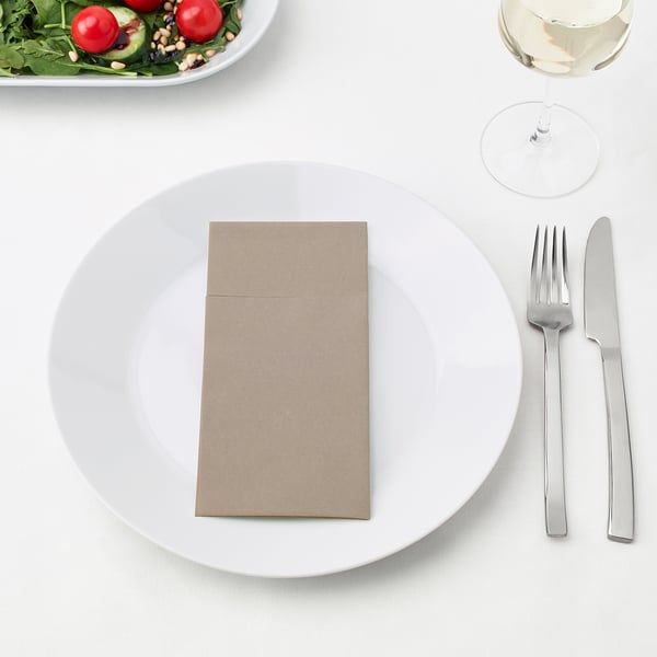 Ein Gedeck mit einem weißen Teller, zwei Metallbestecken, einer gefalteten Serviette und einem Salatbeilage mit einem Weinglas.