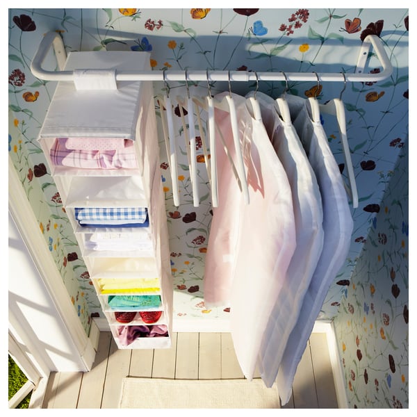 Schrank mit MULIG-Stauraum, Blumentapete, Bettwäsche, heller Holzboden, weiße Tür.