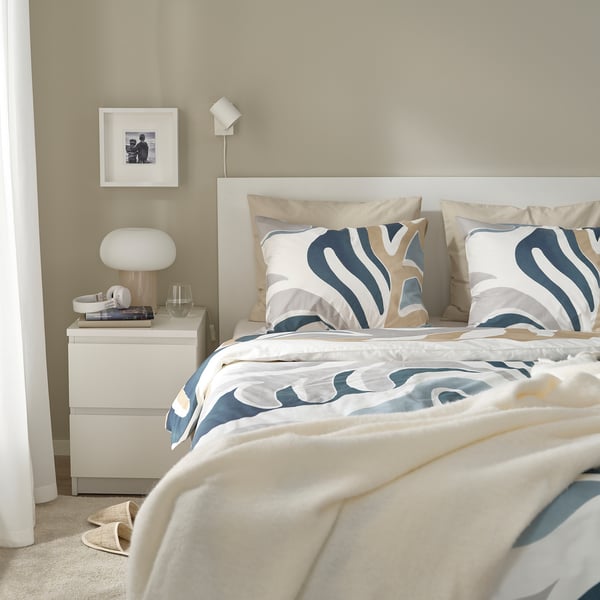 Ein Bett mit MYGGLASVINGE Bettbezugsset in Blau. Großblättriges Design, weiche Baumwoll-Viskose-Mischung. Passend für ein Queensize-/Kingsize-Bett.