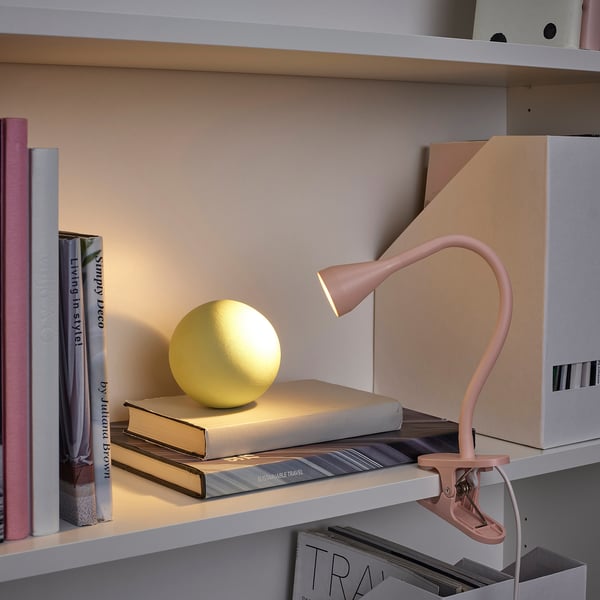 Bücherregal mit NÄVLINGE-Lampe, die eine gelbe Kugel auf gestapelten Büchern beleuchtet.