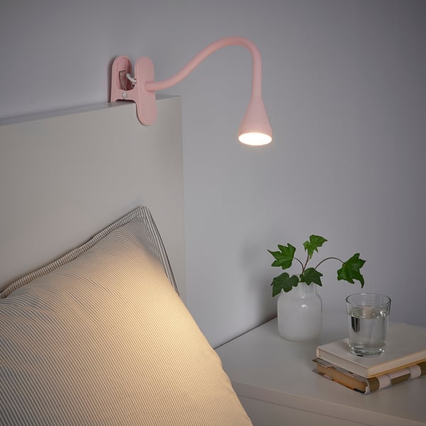 Die wandhängende Nachttischleuchte NÄVLINGE mit flexiblem Hals strahlt warmes, blendfreies Licht auf ein Bett und einen Nachttisch ab.