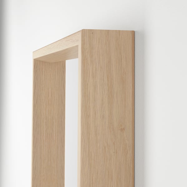 Heller, holzgerahmter Spiegel, der an einer schlichten weißen Wand montiert ist. Einfaches, minimalistisches Design mit klarer Handwerkskunst, die in der polierten Holzmaserung sichtbar ist.