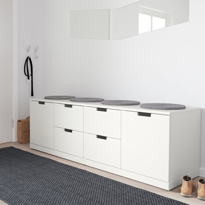 Minimalistische weiße NORDLI-Truhe mit gepolsterten Sitzen, vier runden grauen Hockern, die mit einem schwarz-grauen Teppich und einem einzelnen hellbraunen Stiefel kontrastieren.
