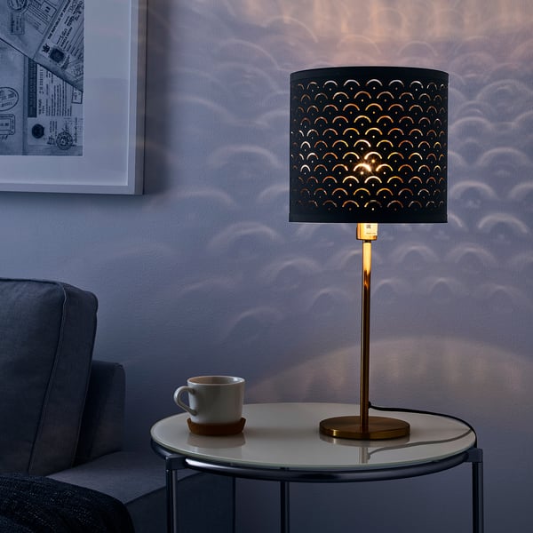 Die Lampe mit verziertem Schirm wirft ein Lichtmuster. Auf dem Tisch neben der Tasse platziert.