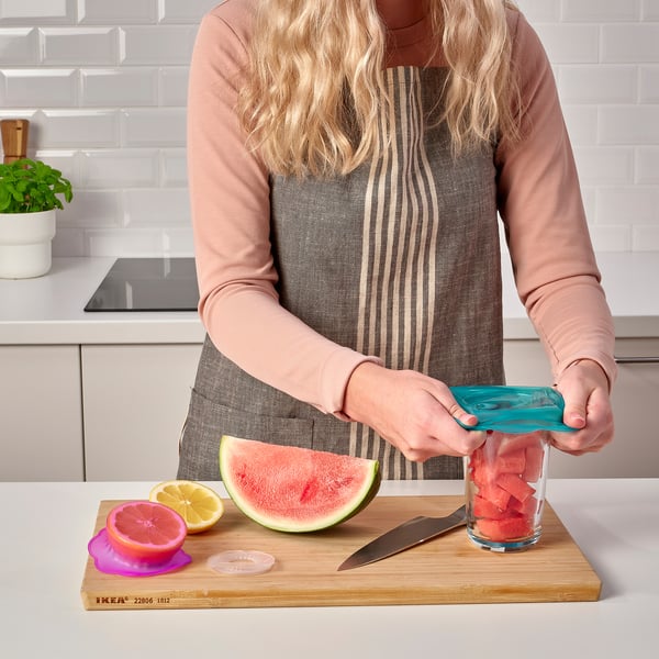 Eine Person verwendet Lebensmittelabdeckungen aus Silikon, um ein Glas mit Wassermelonenstücken zu verschließen. Hebt die Funktion des Produkts hervor, Lebensmittel frisch zu halten.