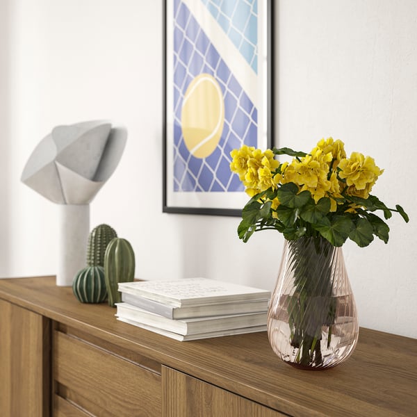 Eine Glasvase mit Wirbeln hält gelbe Blumen auf einem Sideboard, neben einer Lampe und Kakteen.