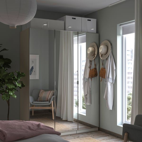 Innenschlafzimmer mit grauem PAX-Kleiderschrank, Spiegeltüren, hängenden Hüten und Taschen, Stuhl in Fensternähe.