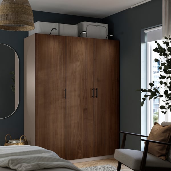 Modernes Schlafzimmer mit großem Holzschrank. Dunkle Wände, helle Bettwäsche, gepolsterte Sitzfläche. Breites Fenster, Pflanzen.