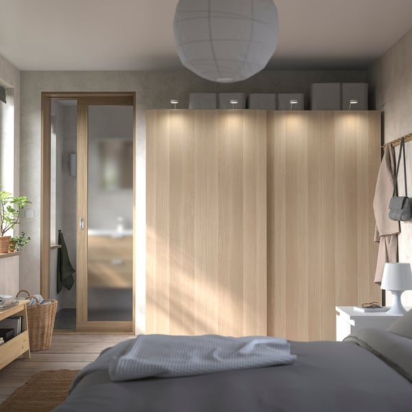 Ein minimalistisches Schlafzimmer mit einem hellen PAX-Kleiderschrank aus Holz, Schiebetüren und integrierter Beleuchtung.