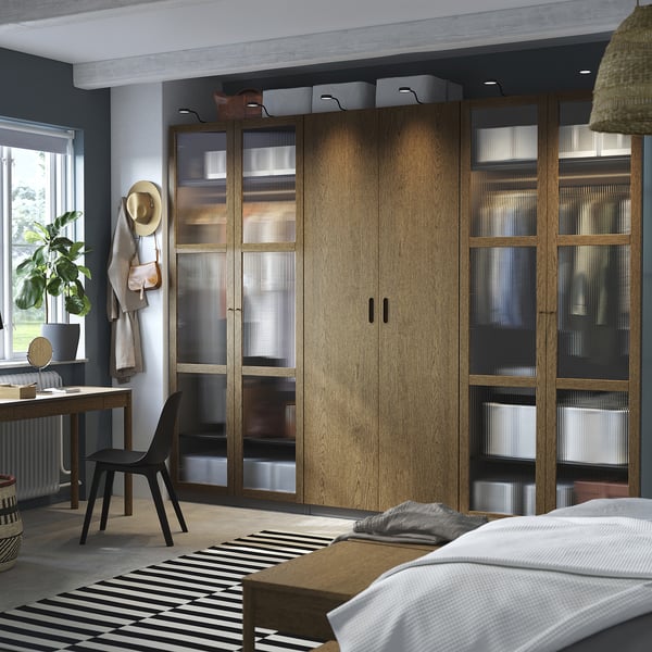 Modernes Schlafzimmer mit großem Holzschrank, Glastüren und schwarzem Stuhl.
