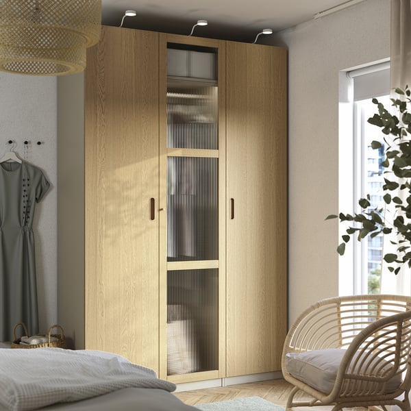 Modernes Schlafzimmer mit großem PAX-Kleiderschrank aus hellem Holz. Gegenüber ein Korbsessel neben einem großen Fenster.