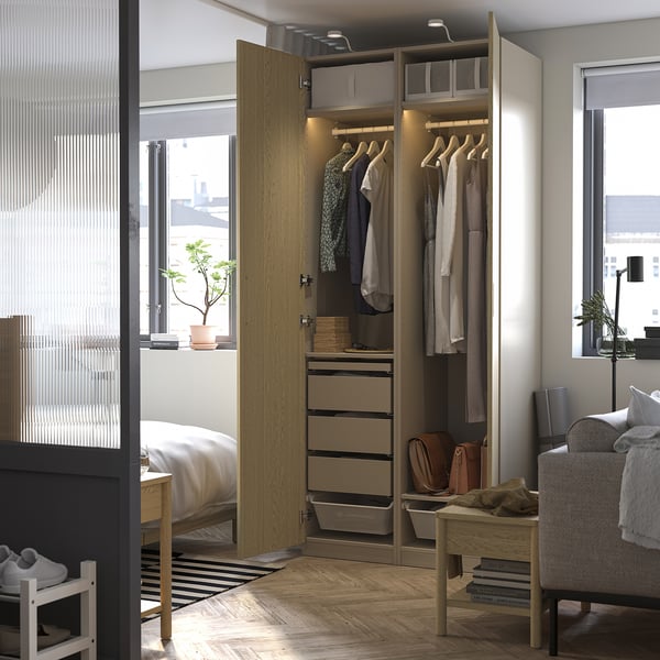 Ein offener PAX-Kleiderschrank aus Holz. Es hängt Kleidung, Schubladen und Aufbewahrungsboxen auf. Ein Licht erhellt den Innenraum.