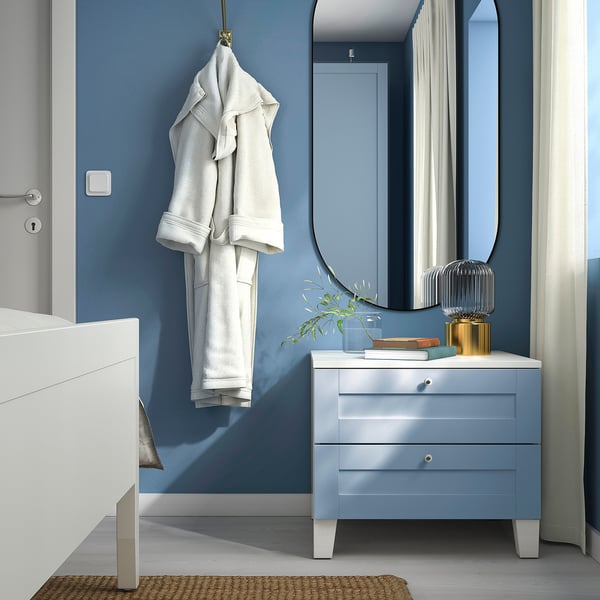 Es ist ein PLATSA Schminktisch in Blau. Hängt Gewand, Spiegel oben, weißer Boden; Ordentlich und gemütlich.