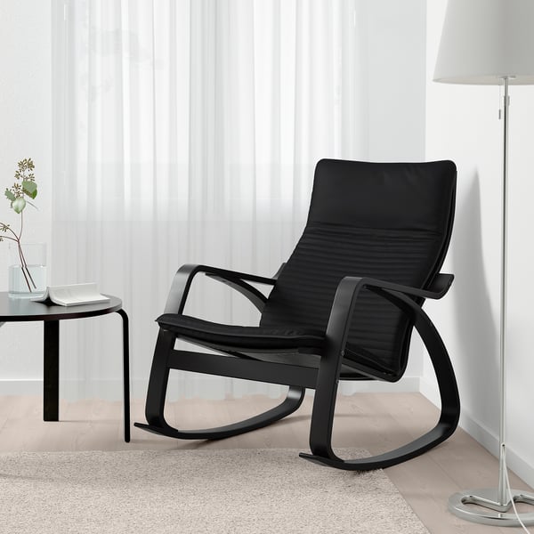 Schwarzer Schaukelstuhl auf einem Teppich, neben einem kleinen Tisch mit Vase und Lampe.
