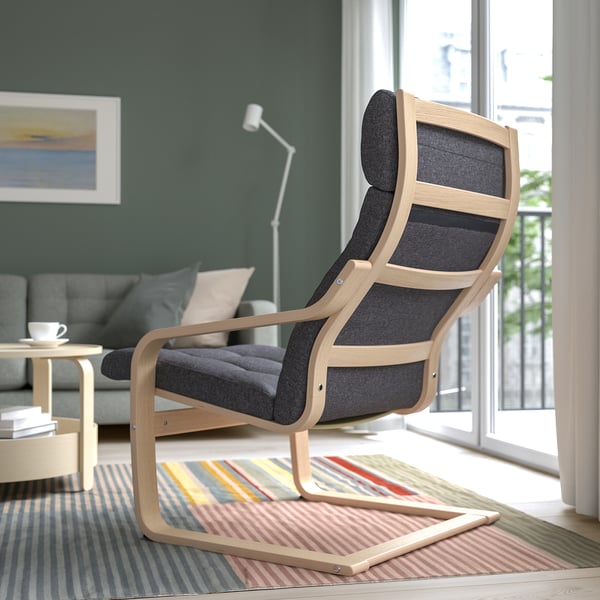 Bequemer Holzsessel mit dunklen Kissen und geschwungener Rückenlehne, der in der Nähe eines bunten Teppichs in einem Wohnzimmer mit Fenster platziert ist.