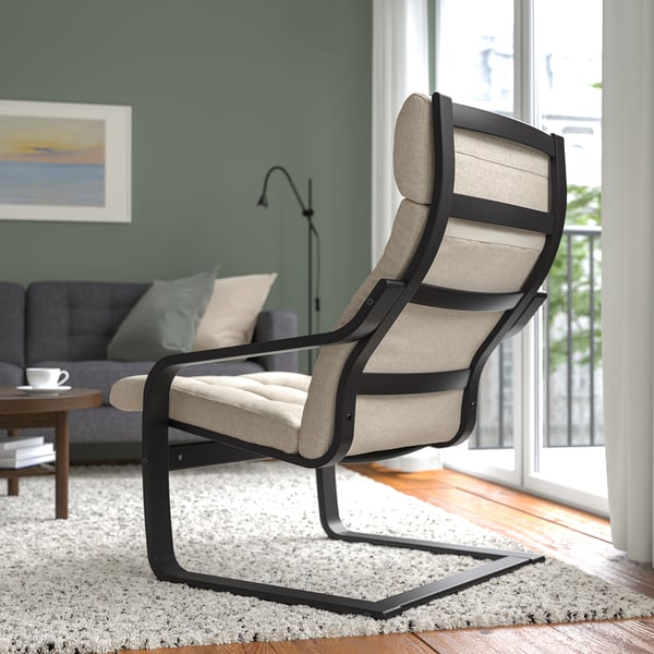 Ein modernes Wohnzimmer mit einem beigegepolsterten, schwarz gerahmten Liegesessel in der Nähe eines großen Fensters, auf einem zotteligen Teppich, neben einem grauen Sofa und einem Couchtisch.