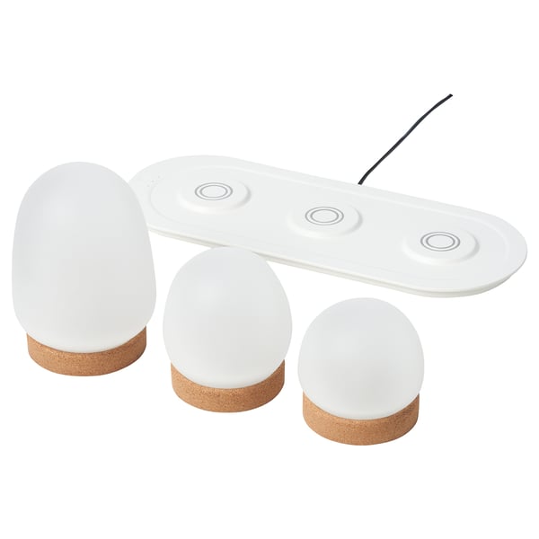 Drei weiße, kugelförmige LED-Lampen auf einer passenden Ladeschale, mit Korksockeln, bieten ein modernes, minimalistisches Design.